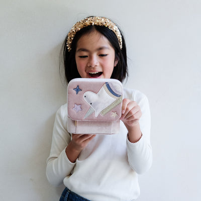 Child holding a pink jewellery box with a unicorn design against a plain background