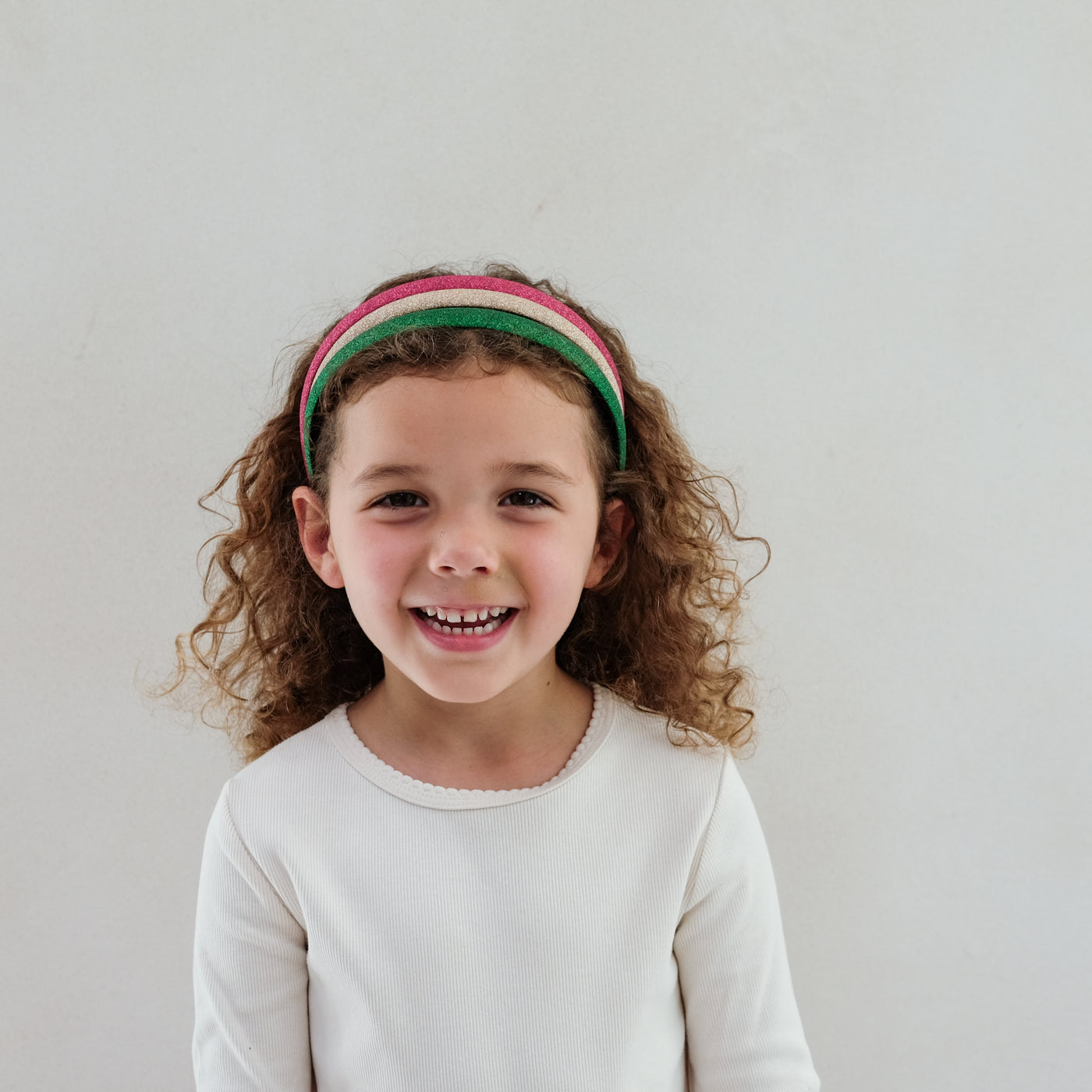 girl with curly hair wearing a pack of three alice bands in Christmas colours on her hair against a white background