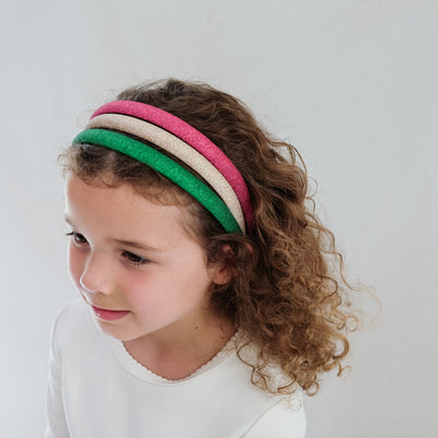 girl with curly hair wearing a pack of three alice bands in Christmas colours on her hair against a white background