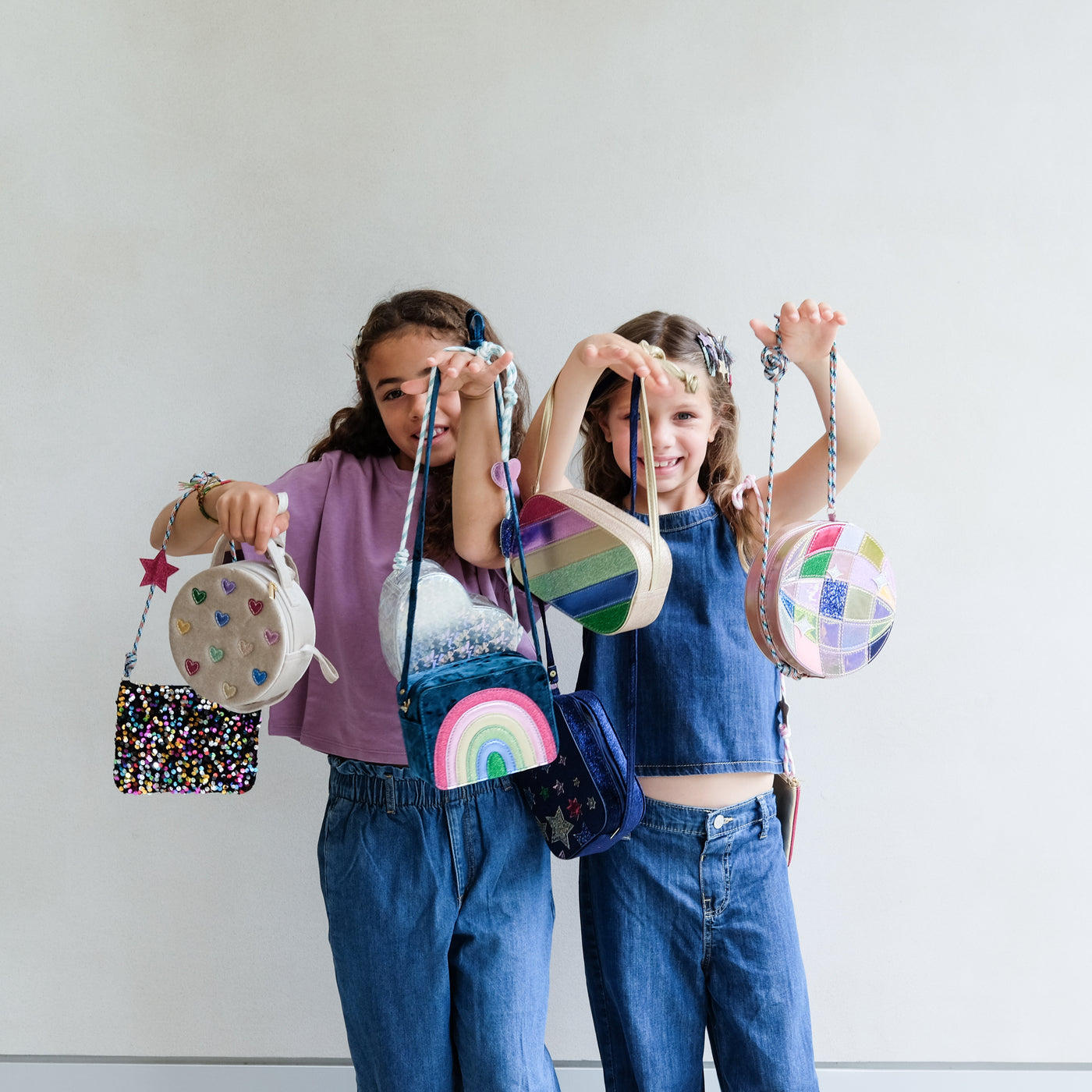 Two children holding colourful handbags against a plain background