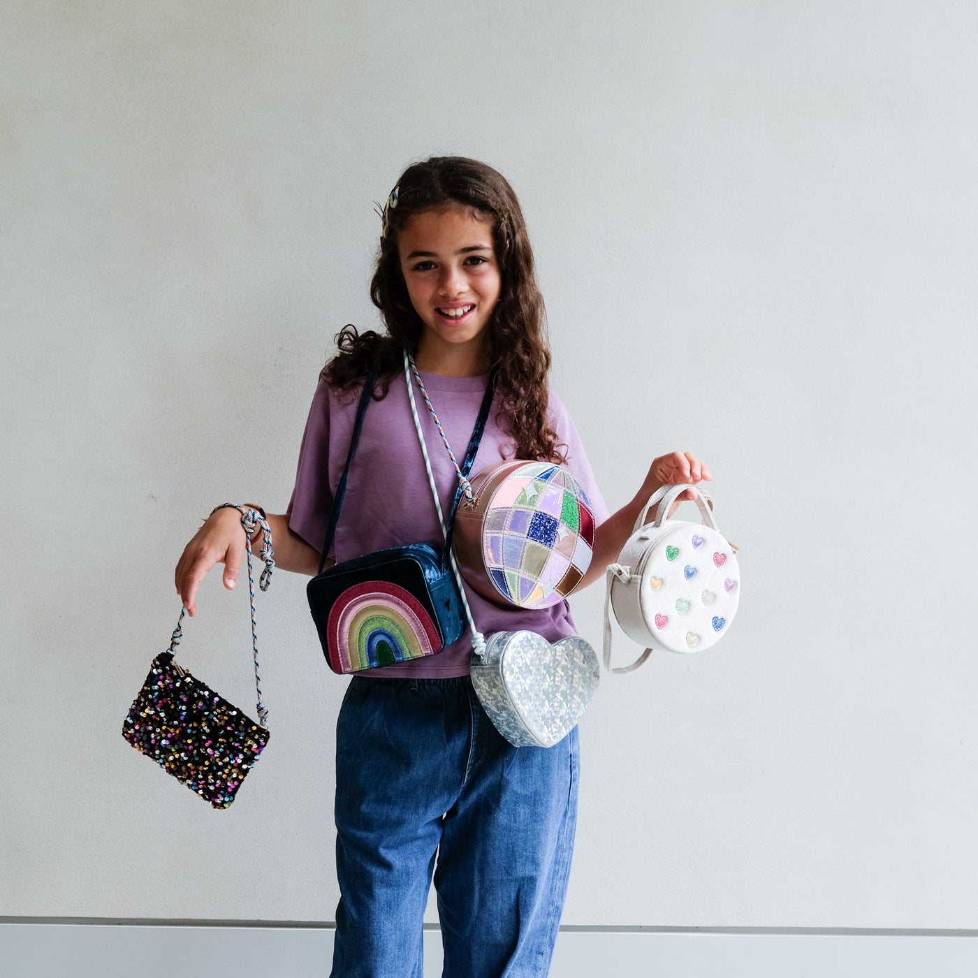 Girl holding various colourful handbags against a plain background