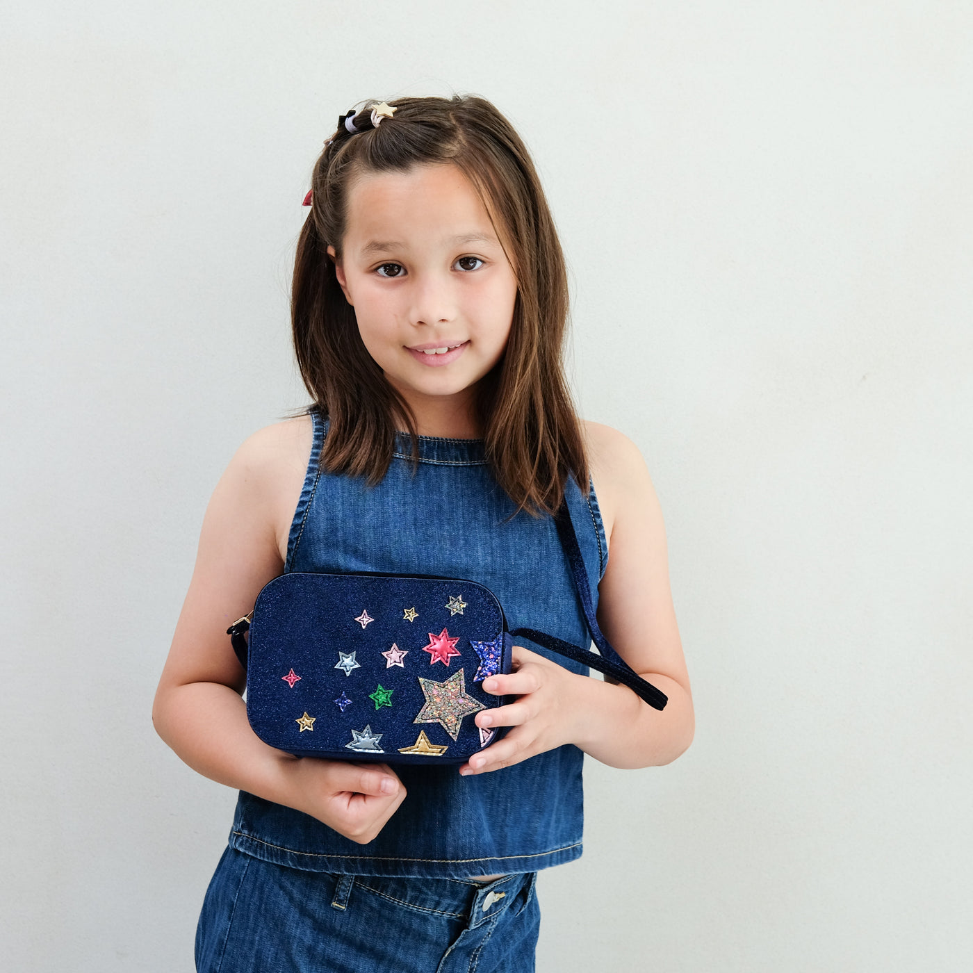 Girl wearing a night sky velvet cross body bag against a plain background