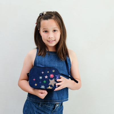 Girl wearing a night sky velvet cross body bag against a plain background
