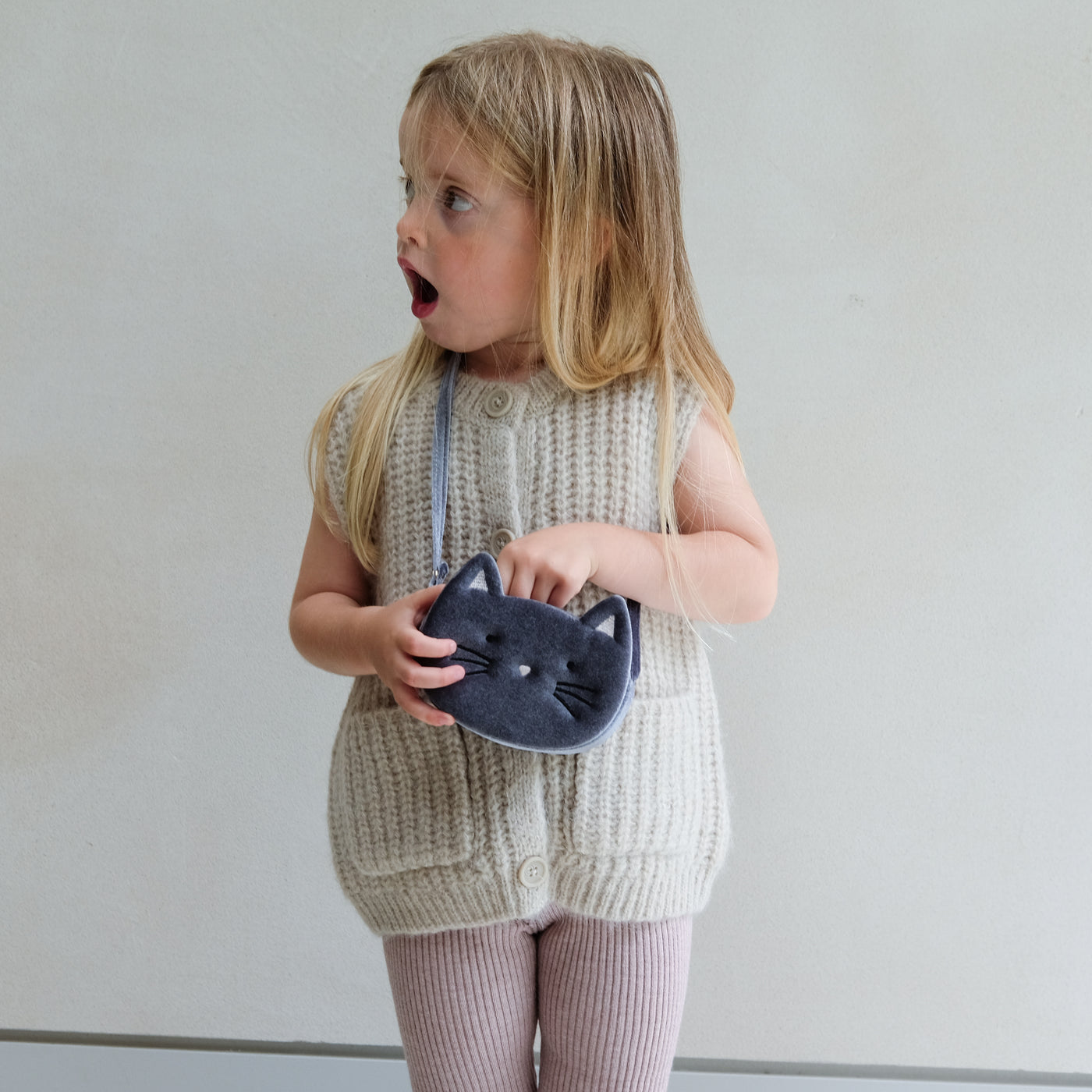 Child holding a grey cat-shaped bag against a plain background