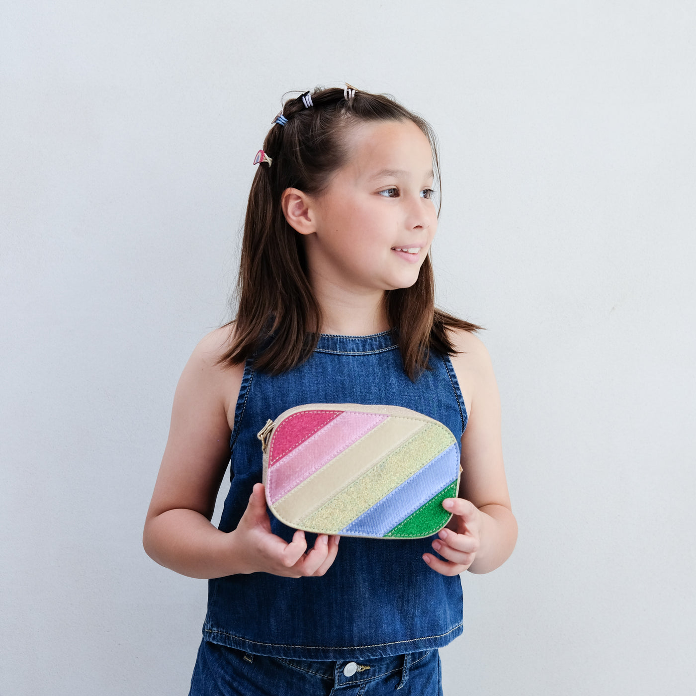 Young girl holding a colourful rainbow striped bag against a plain background