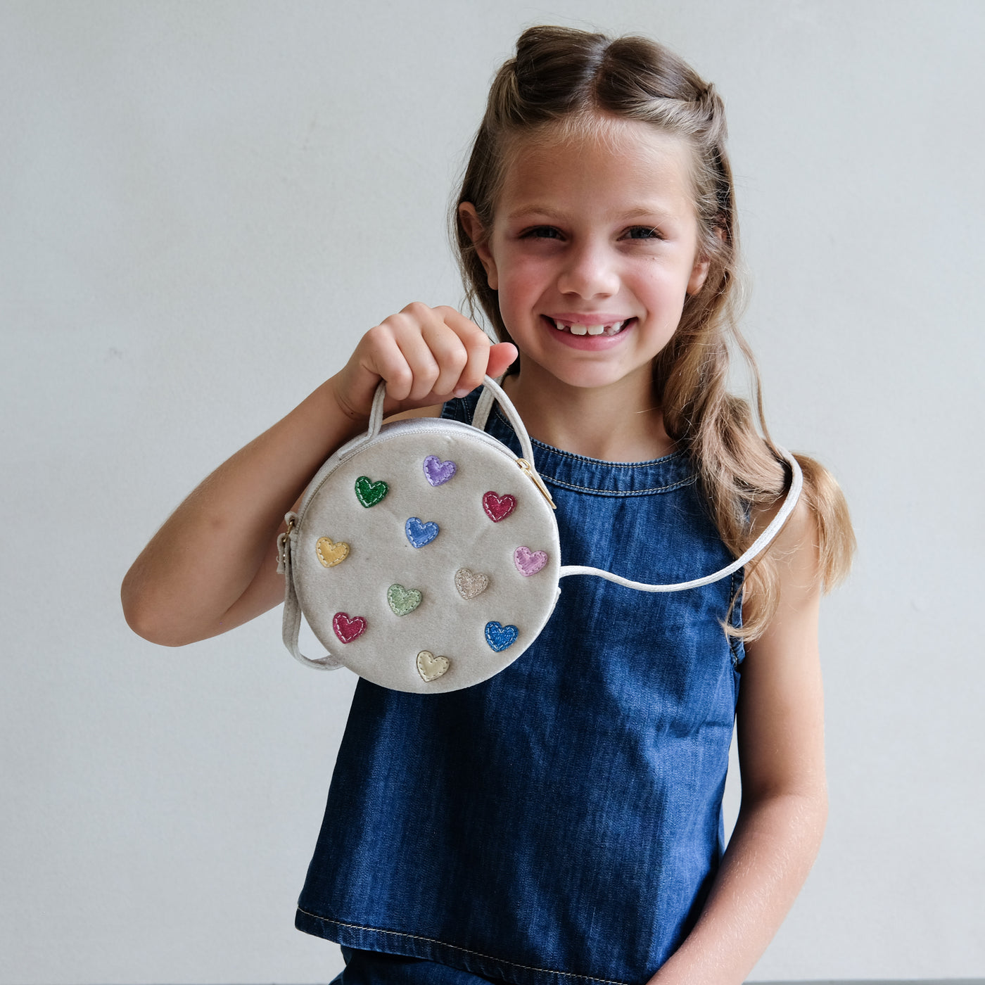 Young girl holding a round bag with heart-shaped decorations against a plain background