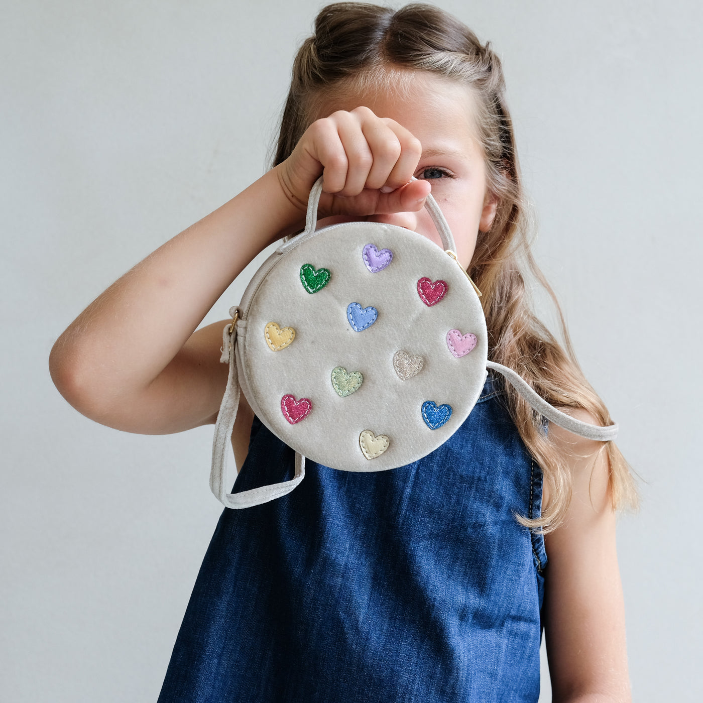 Child holding a round bag with heart-shaped decorations against a plain background