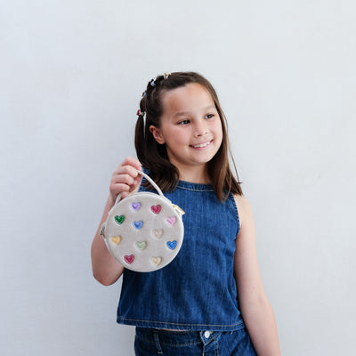 Young girl holding a round bag with heart designs against a plain background