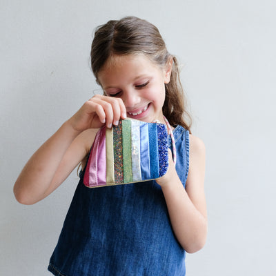 Young girl holding a colourful striped bag against a plain background