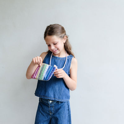 Young girl holding a colourful striped bag against a plain background
