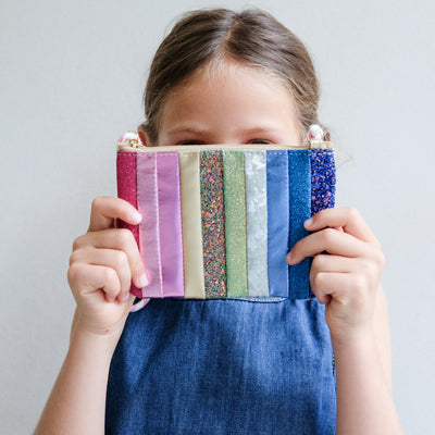 Child holding a colourful striped bag in front of their face against a plain background