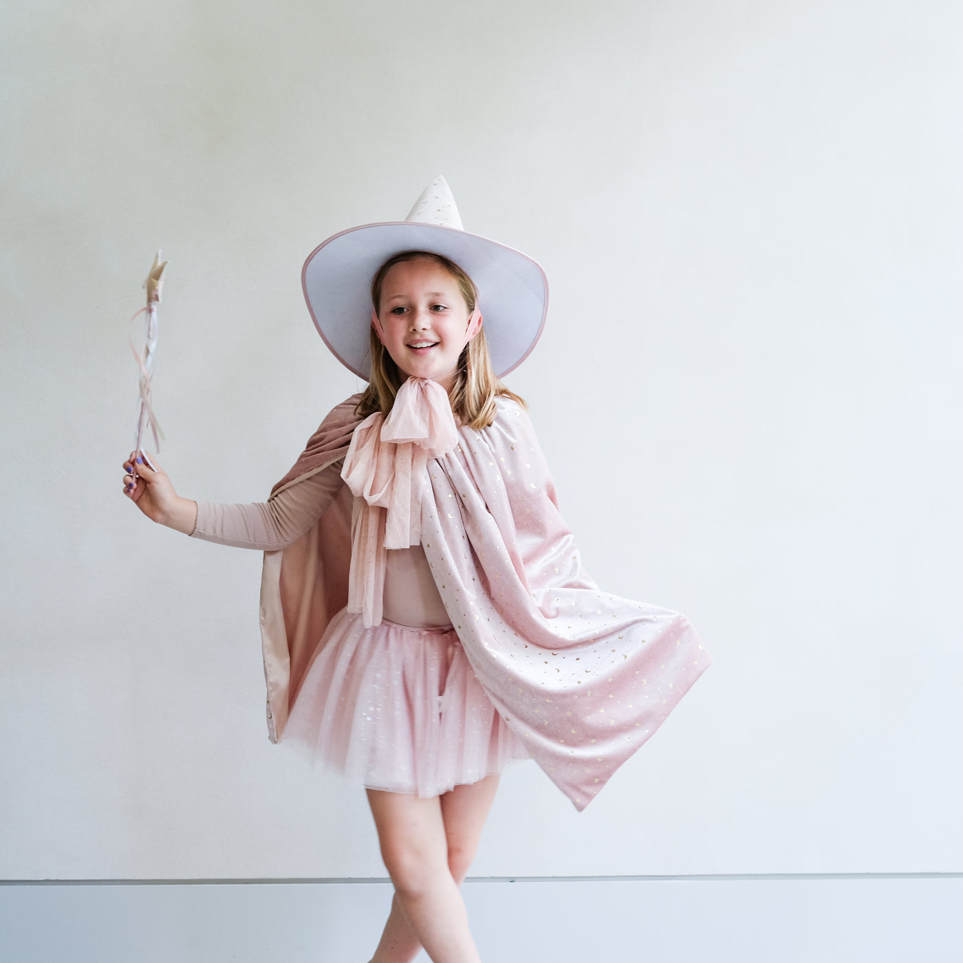 Young girl in a glinda pink witch costume with a white hat against a plain background