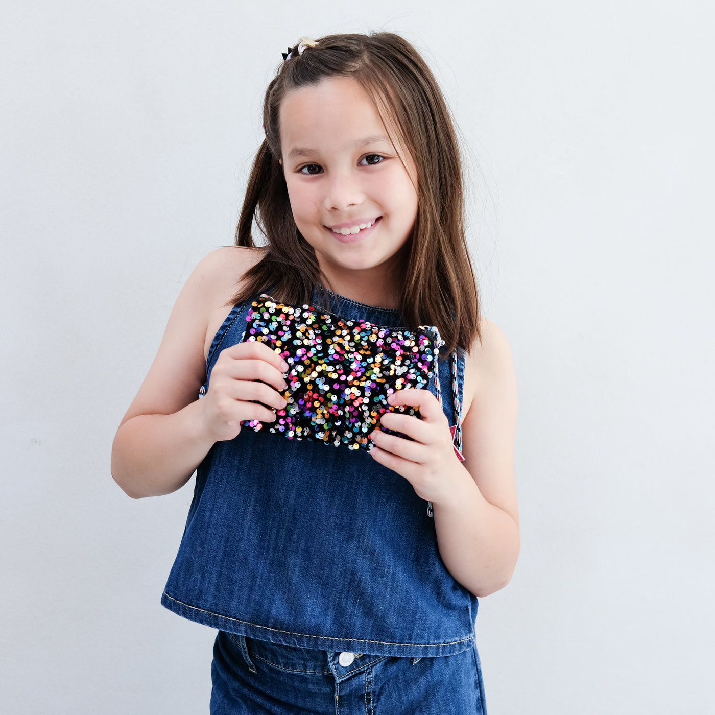 Young girl holding a colourful sequin bag against a plain background