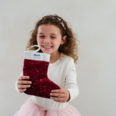 Child holding a red sparkling stocking from mimi & lula against a plain background