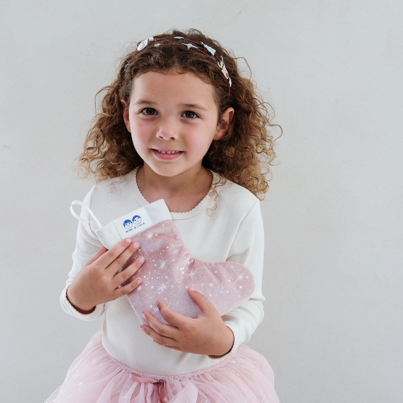 girl holding a pink filled christmas stocking gift against a plain background