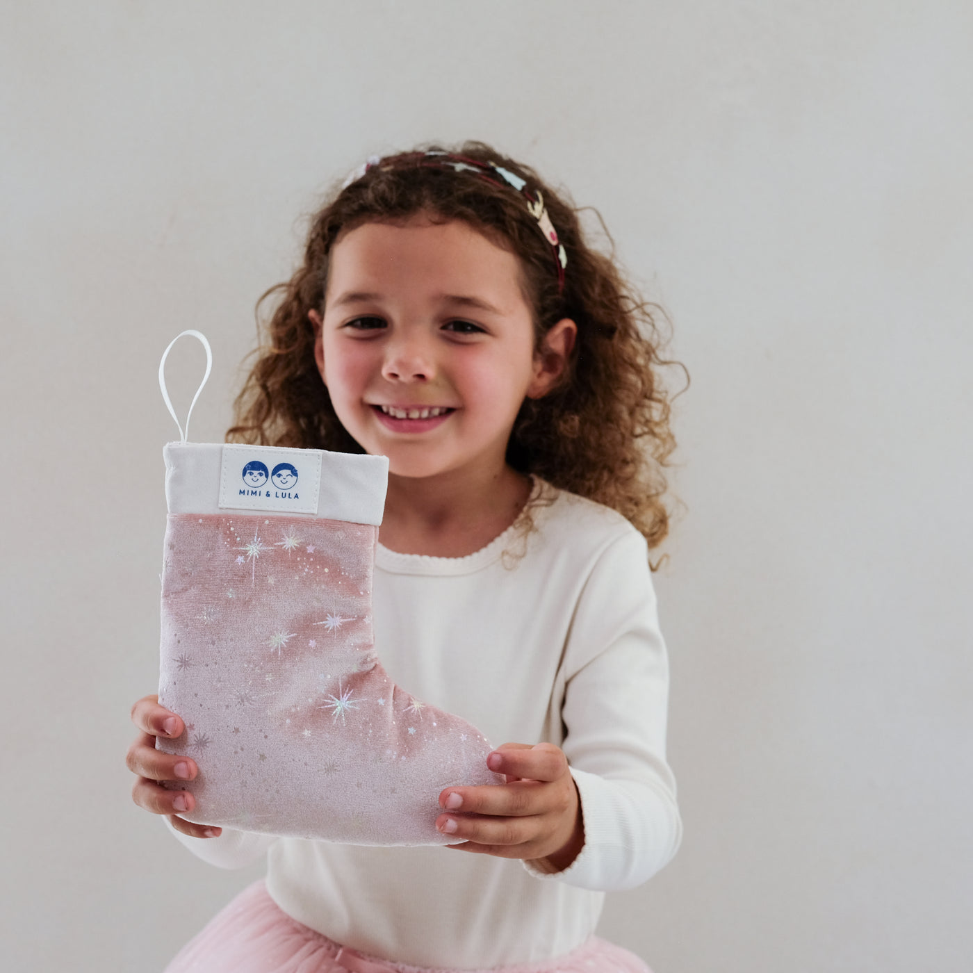 girl holding a pink filled christmas stocking gift against a plain background