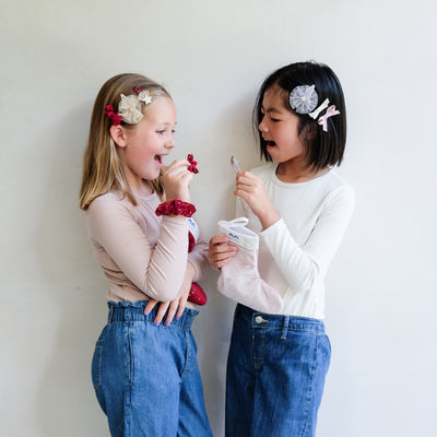 two young girls holding a pink christmas gift stocking and a red christmas gift stocking against a plain white background