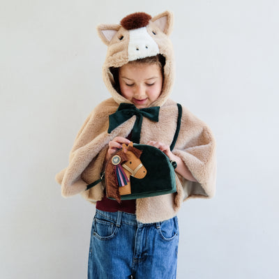 Child wearing a faux fur horse hooded dressing up cape holding a horse novelty cross body bag against a plain background