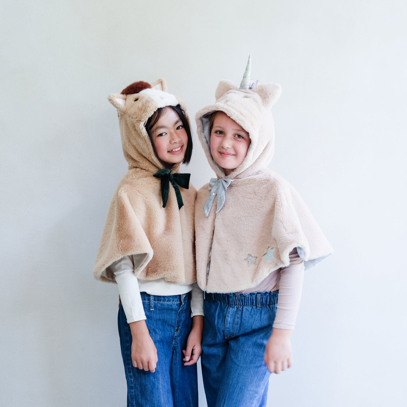 Two children wearing a horse cape and a unicorn cape for dressing up against a plain background