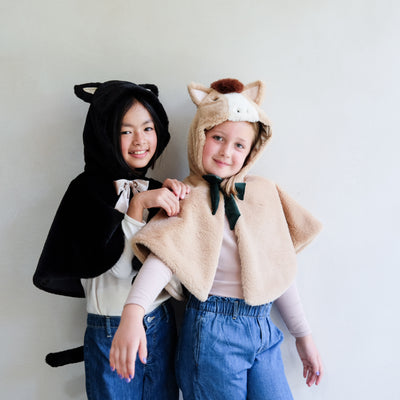 Two little girls in dressing up clothes - one wearing a fluffy black cat cape with hood, ears and tail and one wearing a brown fluffy horse cape with green velvet bow, ears and mane