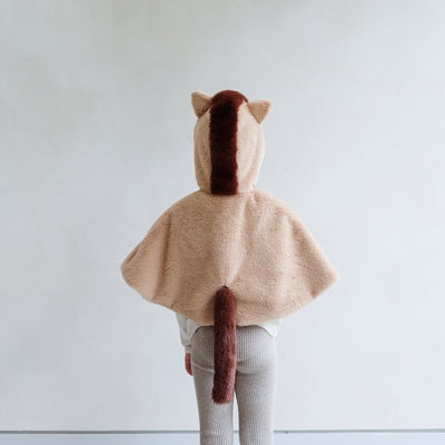 Child wearing a faux fur horse hooded dressing up cape against a plain background