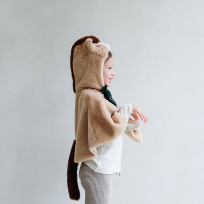 Child wearing a faux fur horse hooded dressing up cape against a plain background