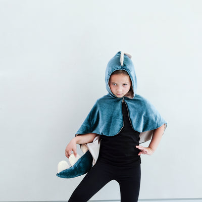 child wearing a velvet dinosaur dressing up cape costume against a white background