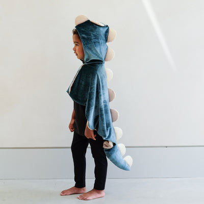 child wearing a velvet dinosaur dressing up cape costume against a white background