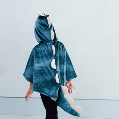 child wearing a velvet dinosaur dressing up cape costume against a white background
