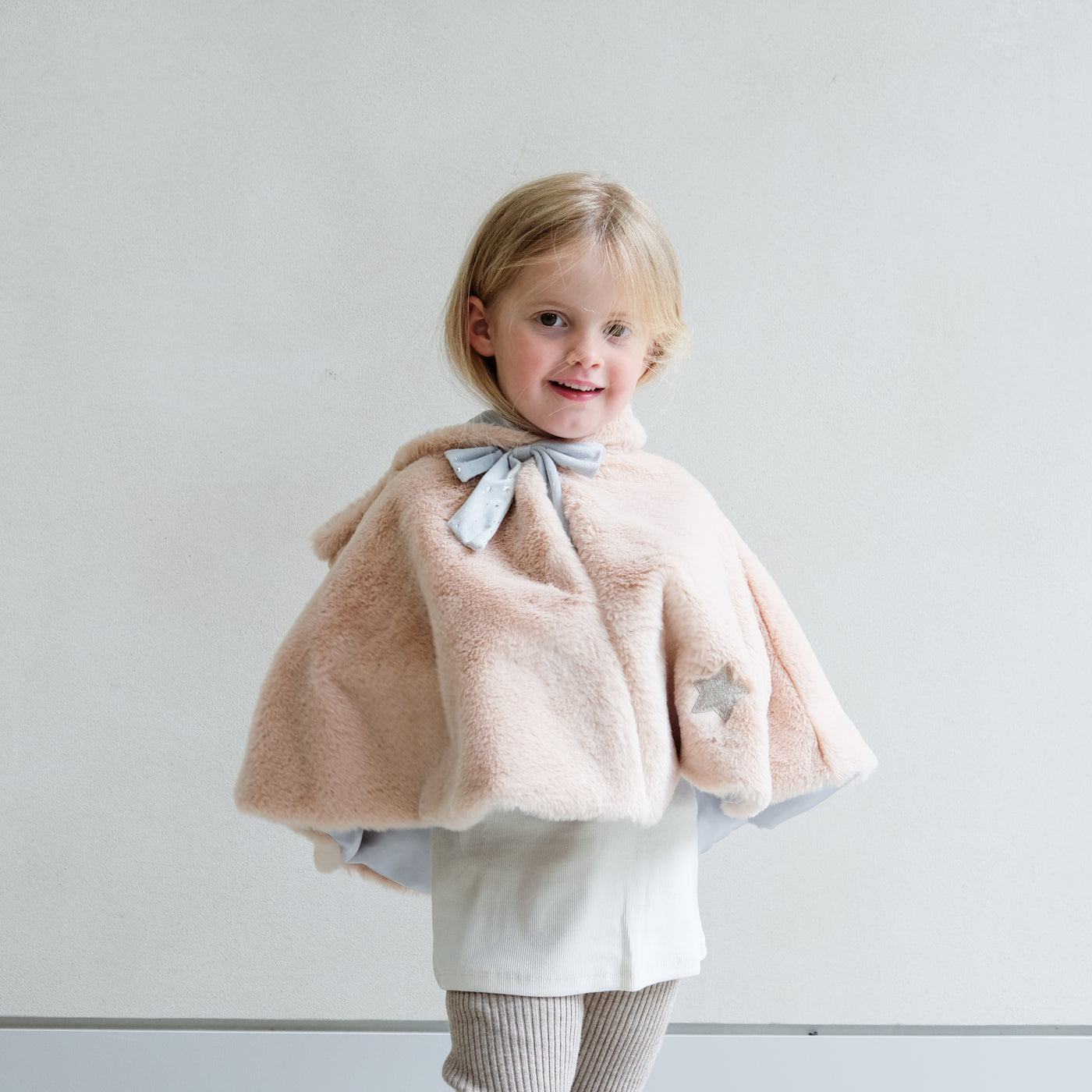 girl wearing fluffy faux fur unicorn dress up cape against a white background