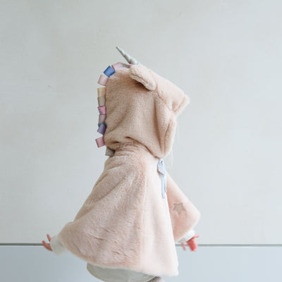 girl wearing fluffy faux fur unicorn dress up cape against a white background