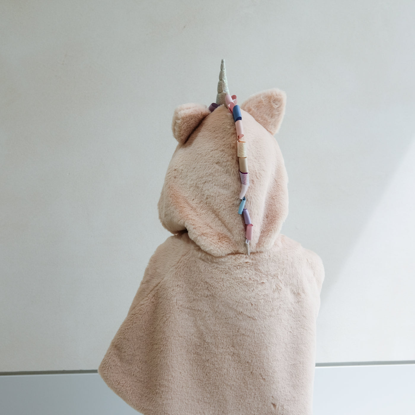 girl wearing fluffy faux fur unicorn dress up cape against a white background