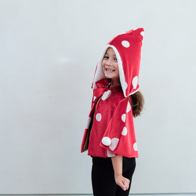 girl wearing a toadstool dressing up red cape, and matching hat against a white background