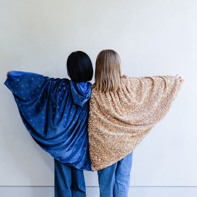 Two people wearing blue and gold capes against a white wall