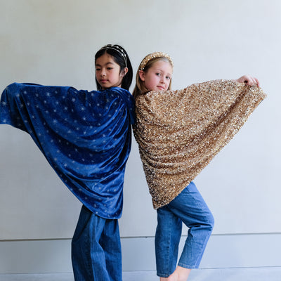 Two children holding up blue and gold capes against a plain background