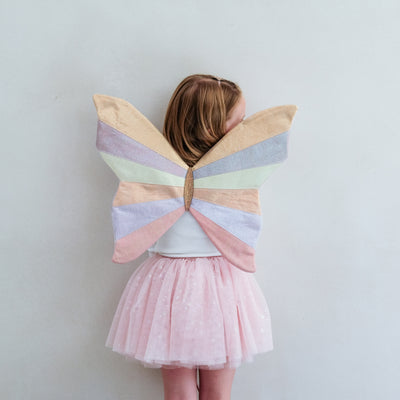 Child wearing a shimmer pink tutu and pink fairy wings with a white background