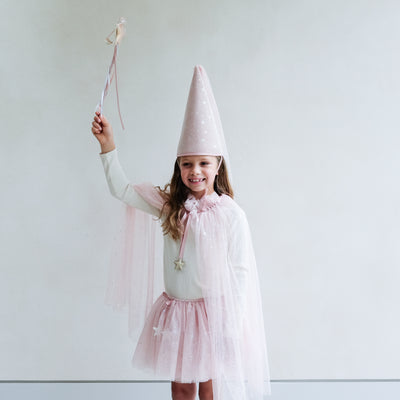 Young girl wearing a full pink shimmer dressing up costume in pink with wand, princess hat, and matching tutu and cape against a white background