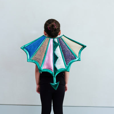 Child wearing a colourful dragon wings costume against a plain background