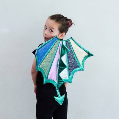 Child wearing a colourful dragon wings costume against a plain background