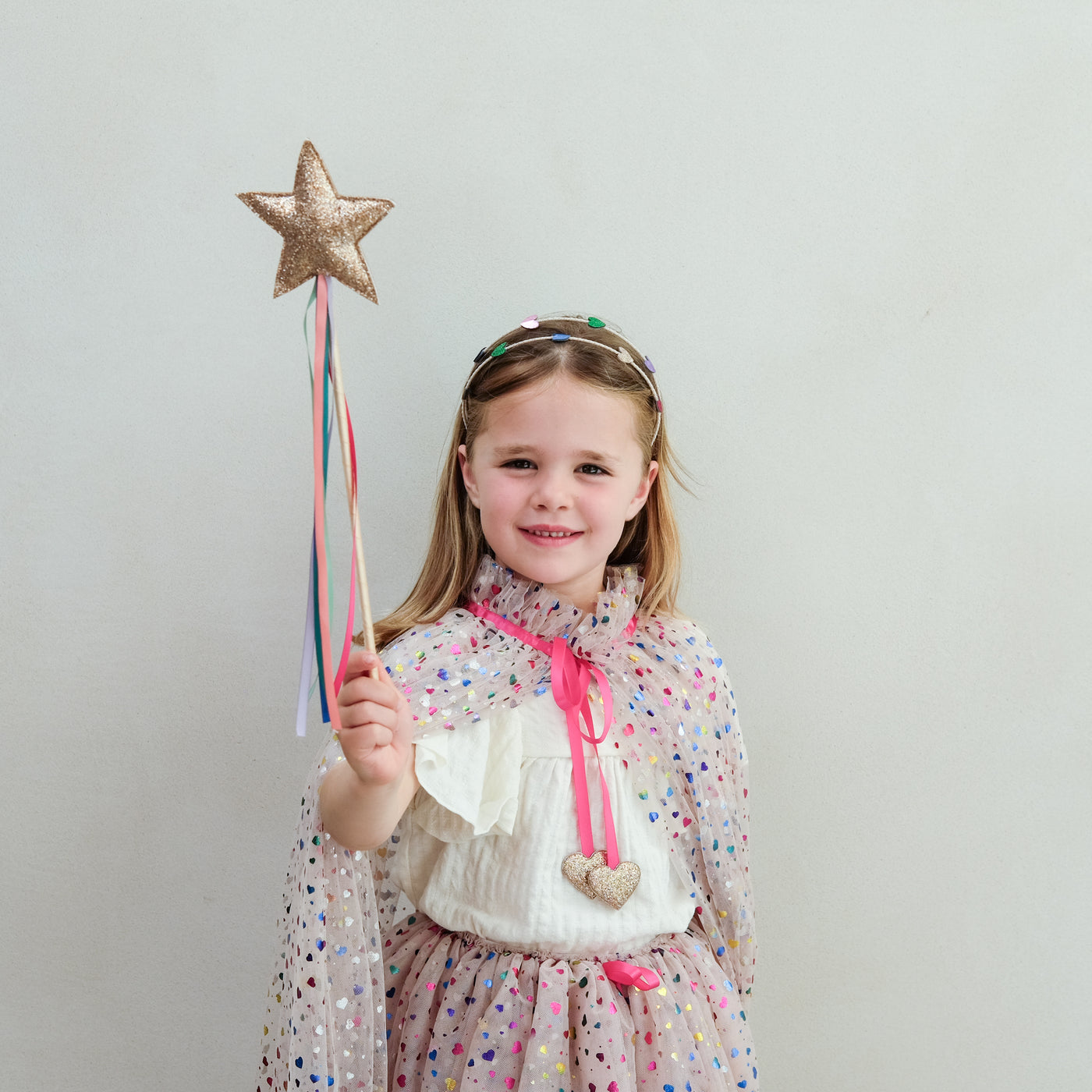 Young girl holding a star-shaped rainbow wand against a plain background