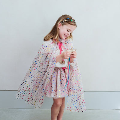 girl wearing rainbow heart cape and rainbow heart tutu against a plain background