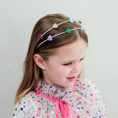 young girl wearing an rainbow heart alice band against a white background