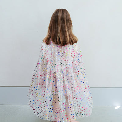 girl wearing rainbow heart cape and rainbow heart tutu against a plain background