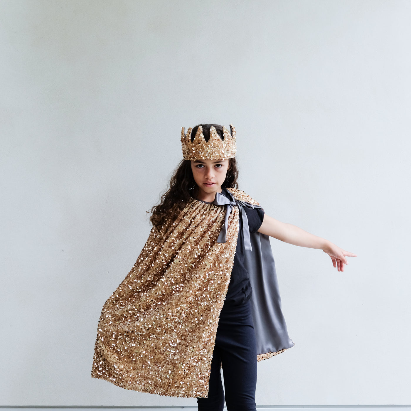 Person wearing a gold sequin cape and gold sequin crown on a white background