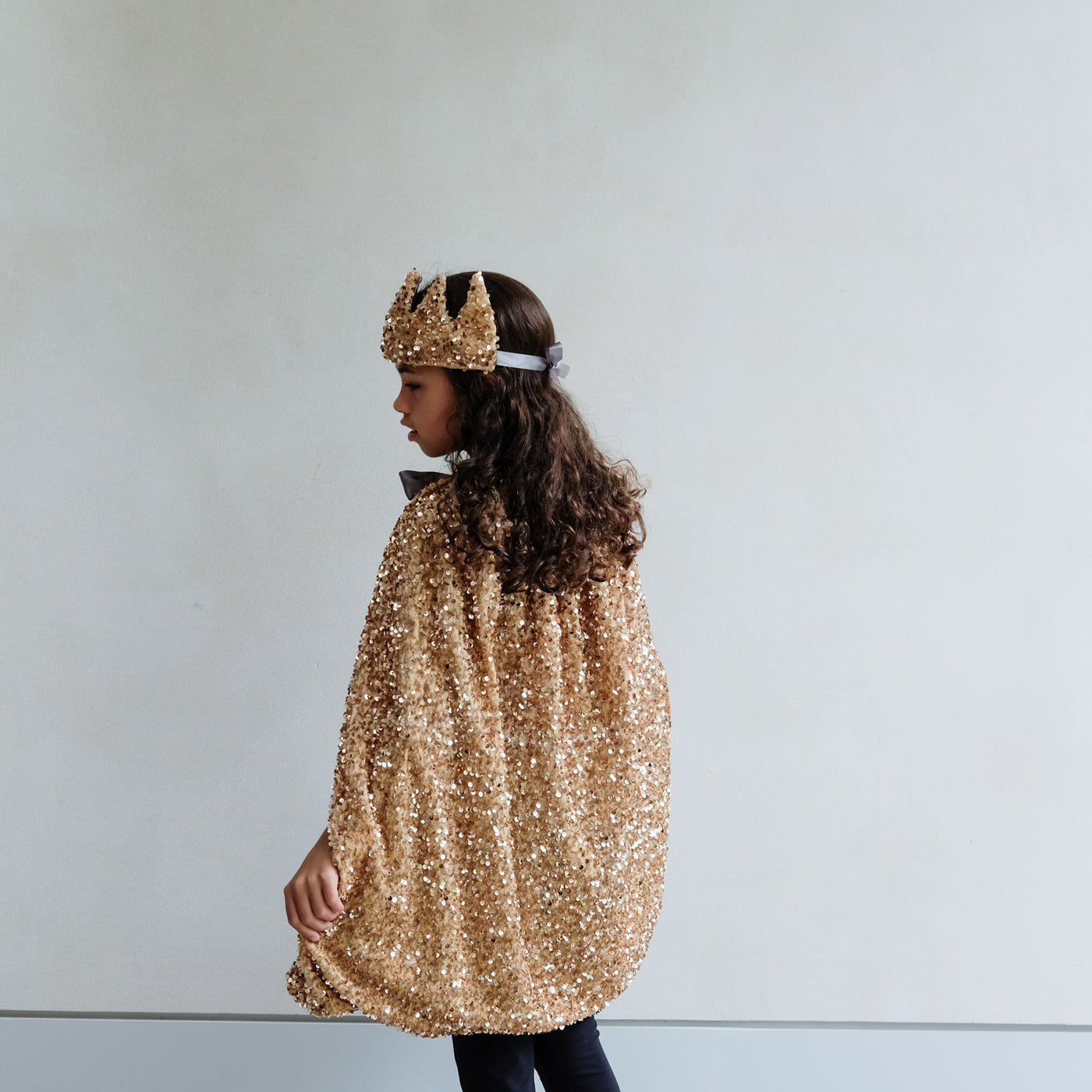 Person wearing a gold sequin cape and gold sequin crown on a white background