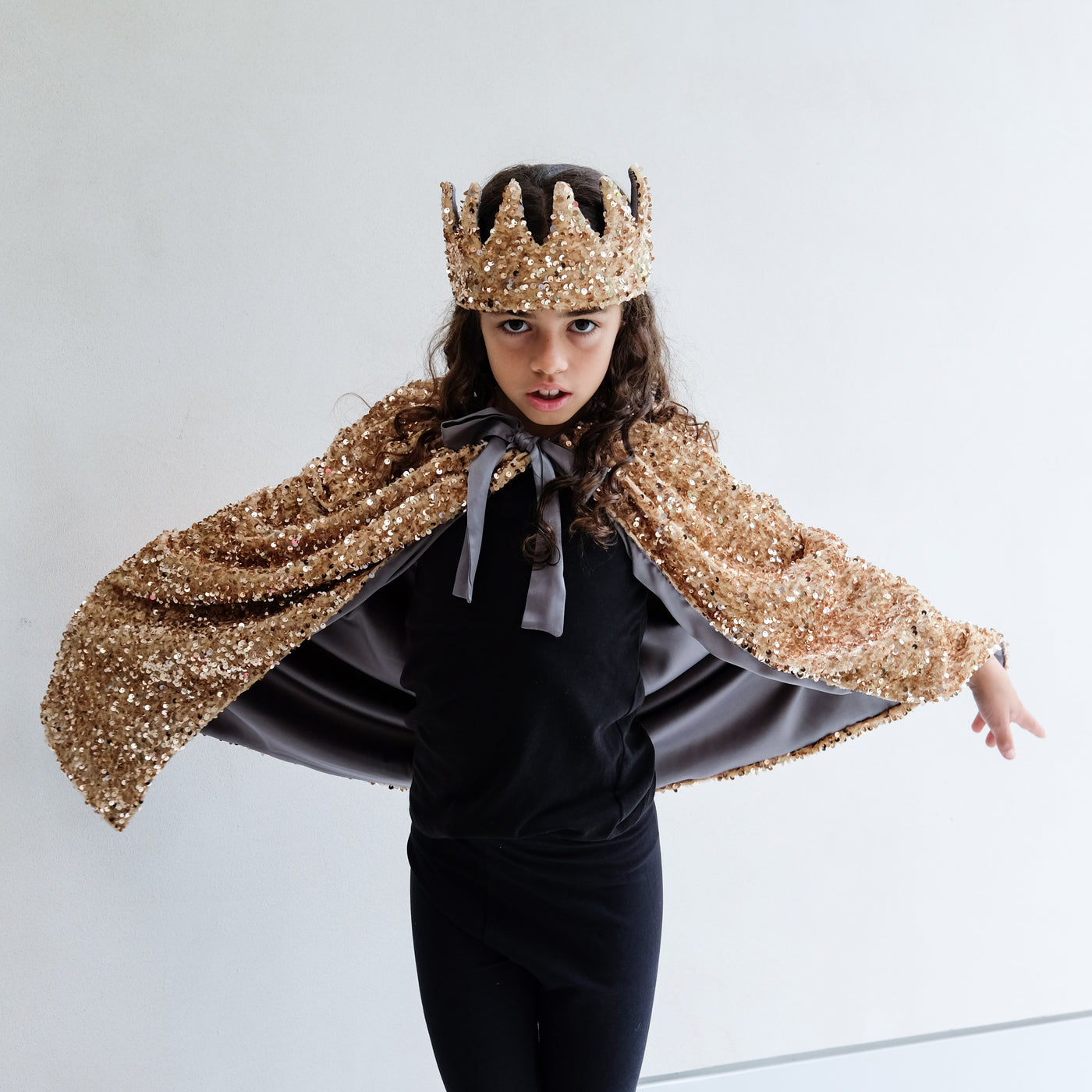 Person wearing a gold sequin cape and gold sequin crown on a white background