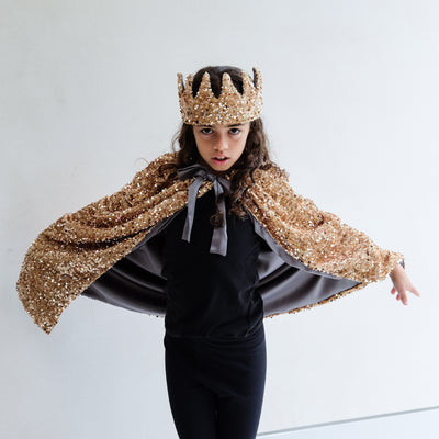 Person wearing a gold sequin cape and gold sequin crown on a white background