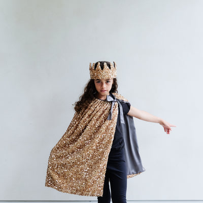 Person wearing a gold sequin cape and gold sequin crown on a white background
