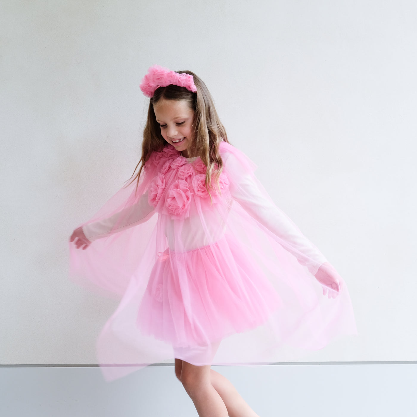 Young girl wearing a pink ruffle floral dressing up outfit and floral headband against a white background
