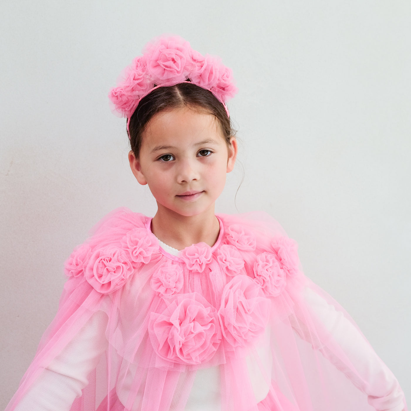 Young girl wearing a pink floral headband and cape against a light grey background
